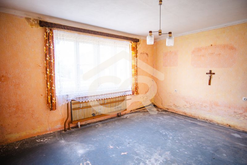 A room in a family house with worn walls, curtains, and a wall crucifix.