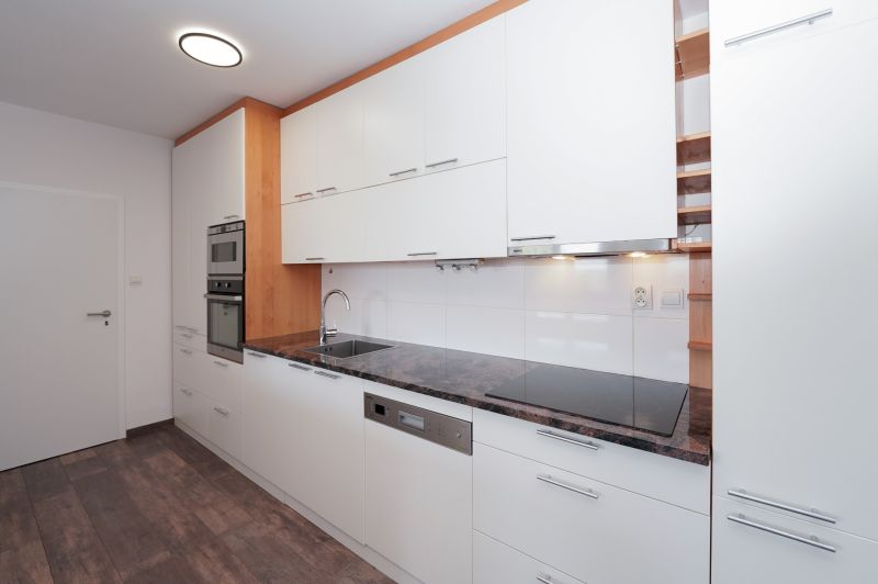 A kitchen in a 3-room apartment with a white kitchen unit and a floor with a wood decor.
