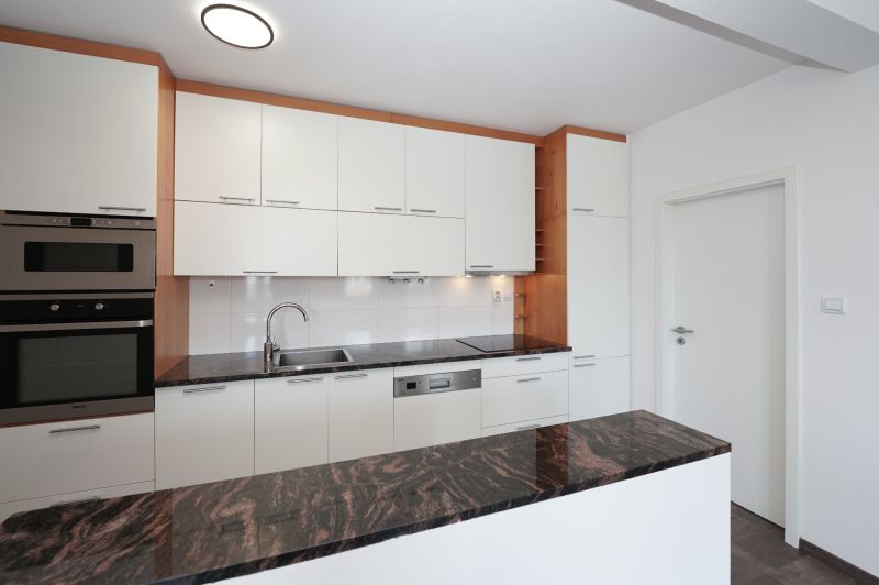 A kitchen in a 3-room apartment with white cabinets and a dark countertop.
