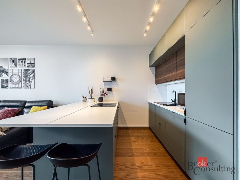A kitchen in a 2-room apartment with a wooden decor floor, modern seating, and minimalist design.