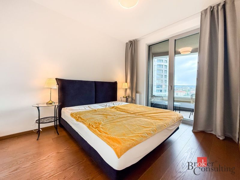 Bedroom in a 2-room apartment with a large bed, wood-patterned flooring, and a balcony.