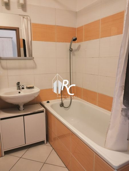 A bathroom in a 2-room apartment with a bathtub and orange-white tiles.