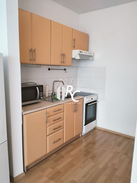 A kitchen in a 2-room apartment with a wooden decor floor, a microwave, and a stove.
