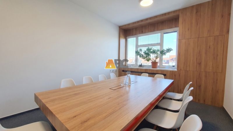 Office with a large table and chairs, floor with wooden decor, window with a plant.