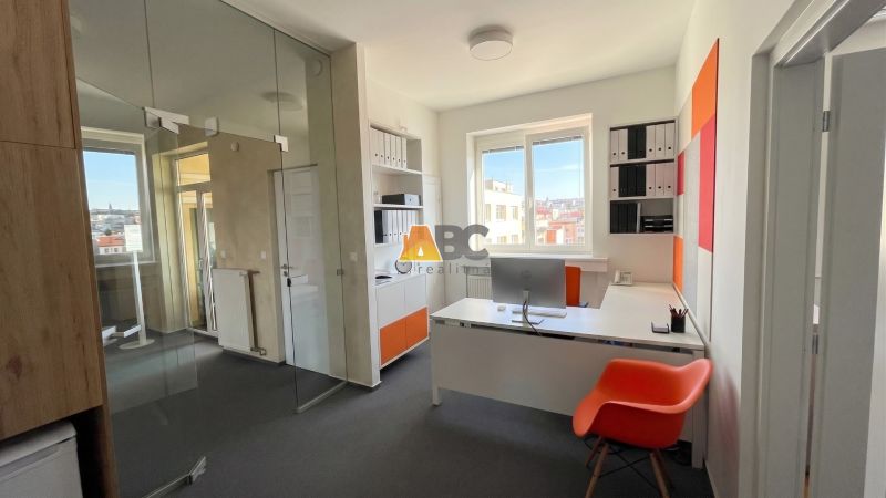 Offices with a glass partition, a desk, an orange chair, and a view from the window.