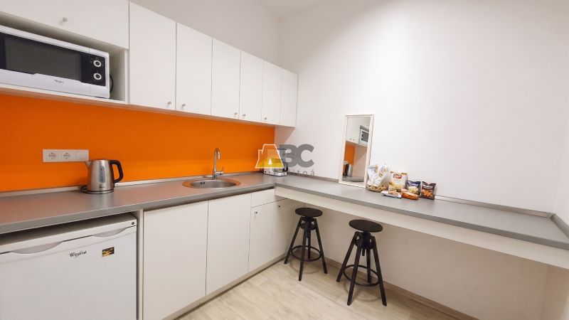 Offices with a kitchenette, white cabinets, an orange wall, and a wood-patterned floor.