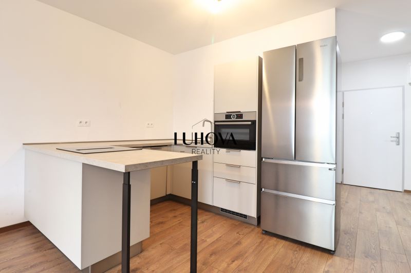 A kitchen in a studio apartment with a stainless steel refrigerator and wood-patterned flooring.