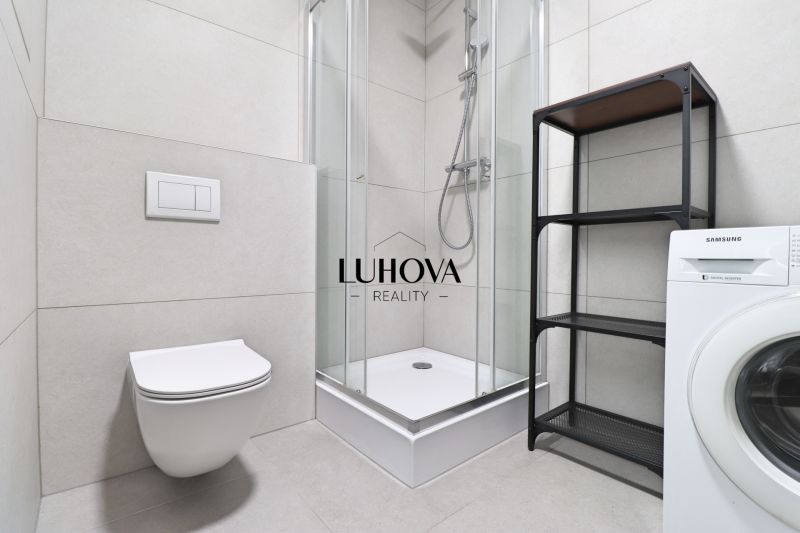 A bathroom in a studio apartment with a toilet, shower, and washing machine.