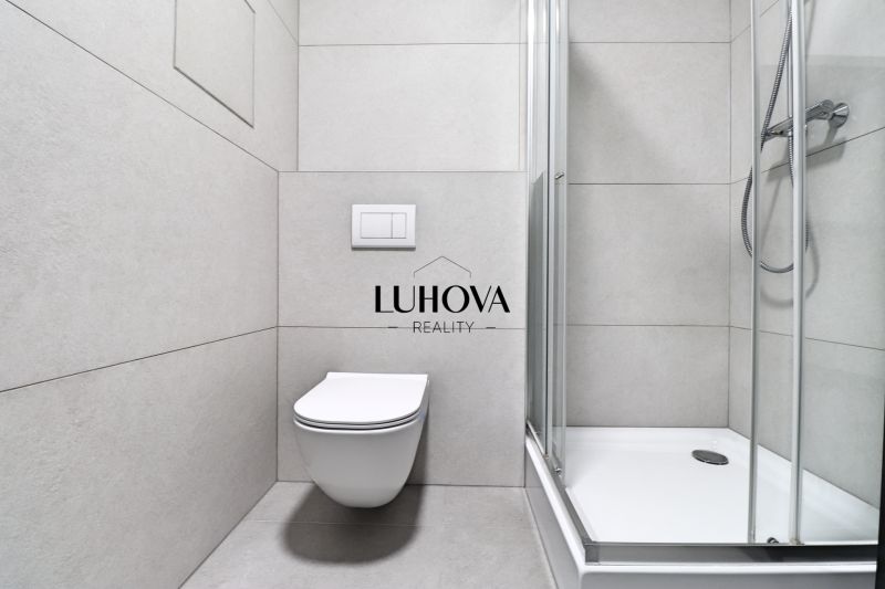 Bathroom with toilet and shower in a studio apartment, with neutral tiles.
