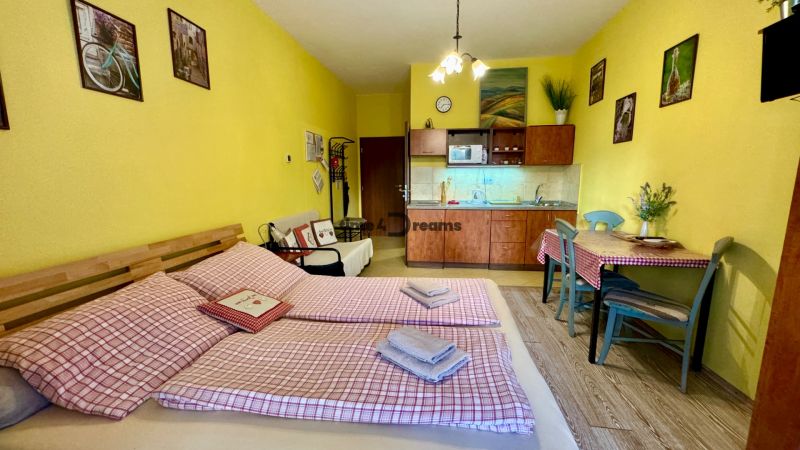 Yellow walls, kitchen unit, dining table, bed, and floor with wooden decor in the Holiday Apartment.