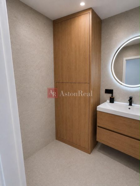 Bathroom with wooden furniture in a 2-room apartment, round mirror above the sink.