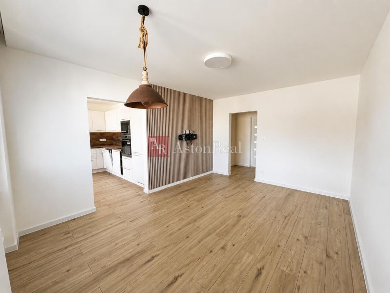 Living room with wood-patterned flooring connected to the kitchen in a two-room apartment.