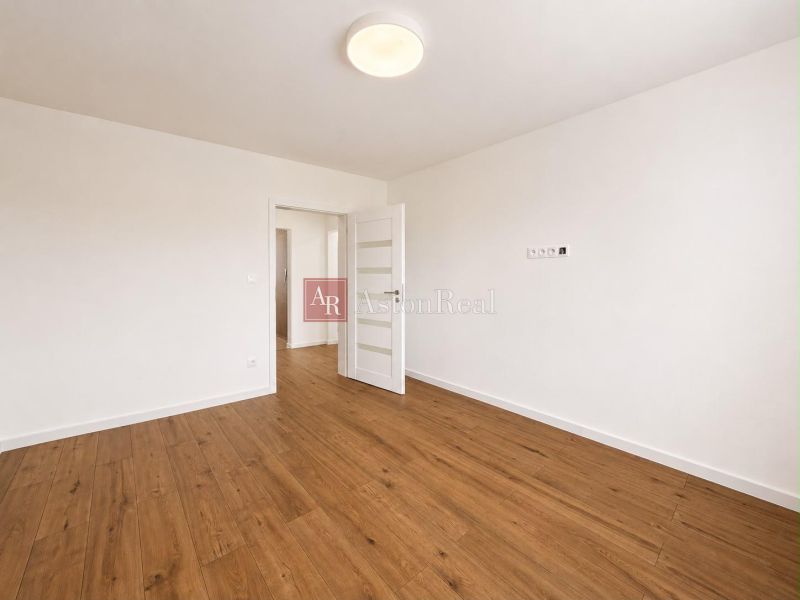 Spacious room in a 2-room apartment with wood-patterned flooring and white walls.