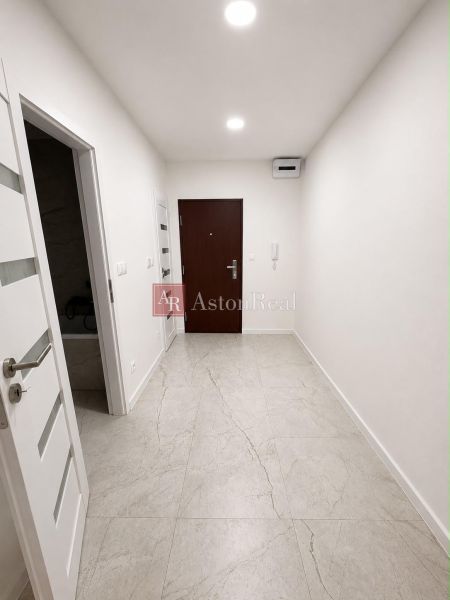 A bright hallway with a light floor in a 2-room apartment, white walls, and wooden doors.