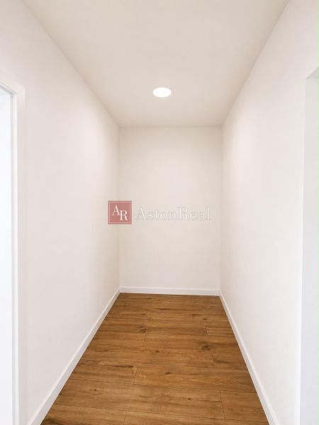 A hallway with white walls and a wooden decor floor in a 2-room apartment.