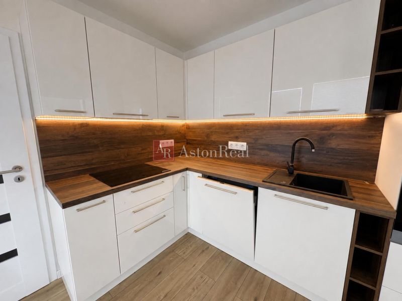 A kitchen in a 2-room apartment with white cabinets and a wooden decor floor.