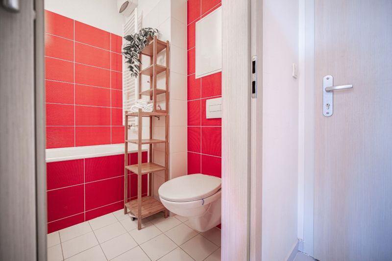 Bathroom in a 2-room apartment with red tiles and a wooden shelf.