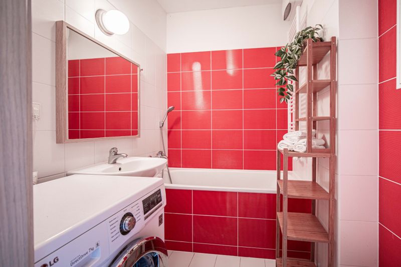 The bathroom in the 2-room apartment features red tiles, a bathtub, and a washing machine.