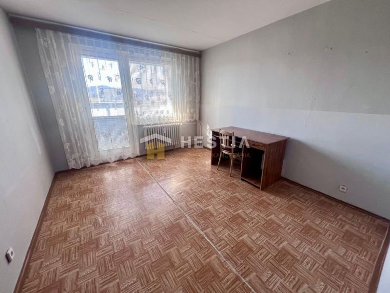 A room in a 3-room apartment with a wooden decor floor and a table by the window.