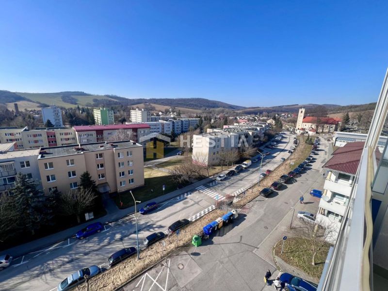 A street with cars and apartment buildings, surrounded by hills in Brezová pod Bradlom.