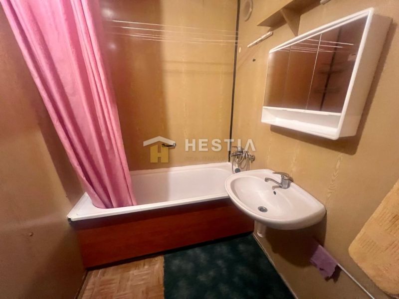A bathroom in a 3-room apartment with a bathtub and a pink curtain, a white sink, and a cabinet.