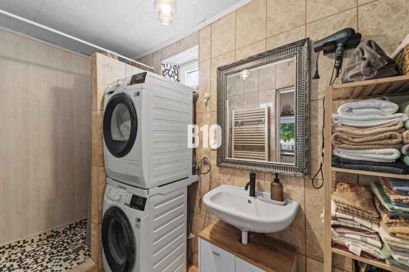 A bathroom in a family house with a shower, a washing machine, a dryer, and shelves with towels.