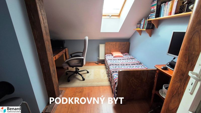 Attic room with a bed, chair, computer, and books, floor with wooden decor.