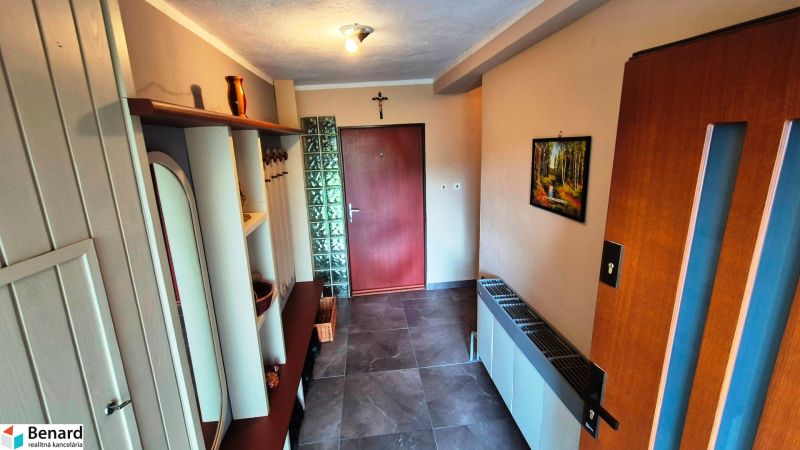 A hallway in a family house with a coat rack wall and tiles, a picture of nature on the wall.