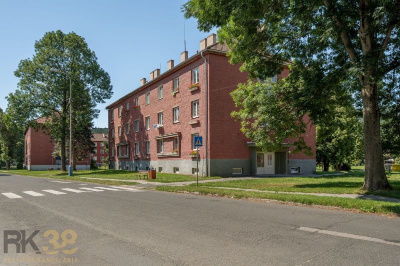 Brick apartment building with three floors in Poprad surrounded by greenery and a bench.