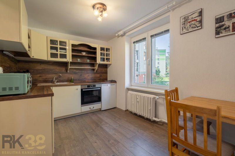 A kitchen in a studio apartment with a wood-patterned floor, light cabinets, large window.