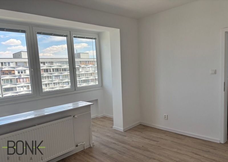 A bright room with large windows and a wooden decor floor in a 2-room apartment.