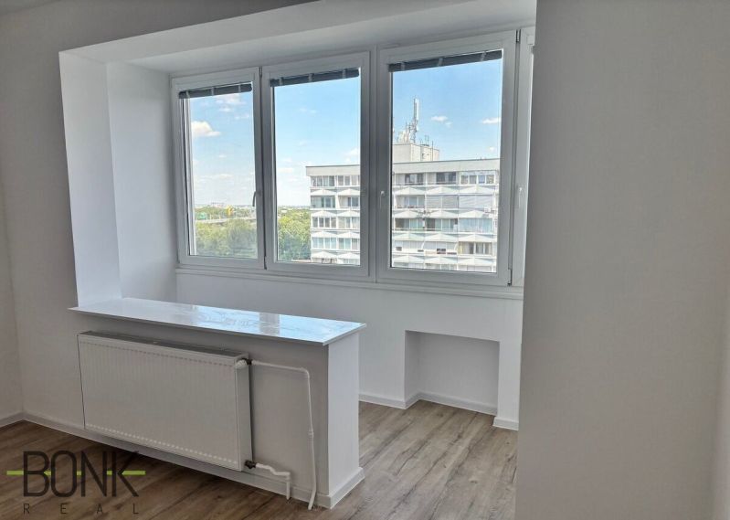 A bright room in a 2-room apartment with a wood-patterned floor and a large window.