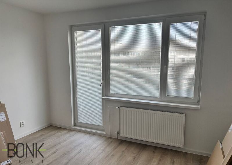A room with a wooden floor design, windows with blinds, a radiator in a 2-room apartment.