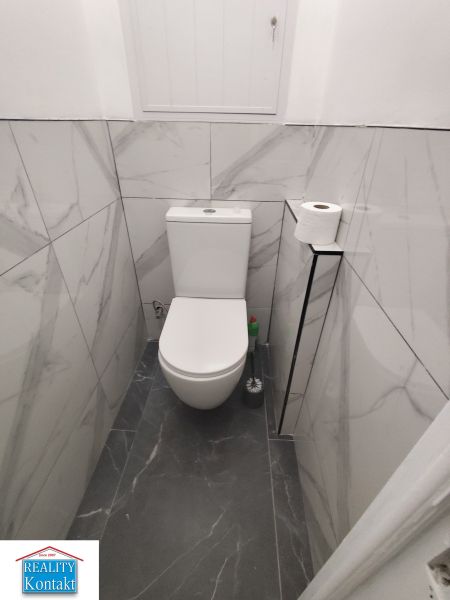 A toilet in a 3-room apartment with marble tiles on the walls.