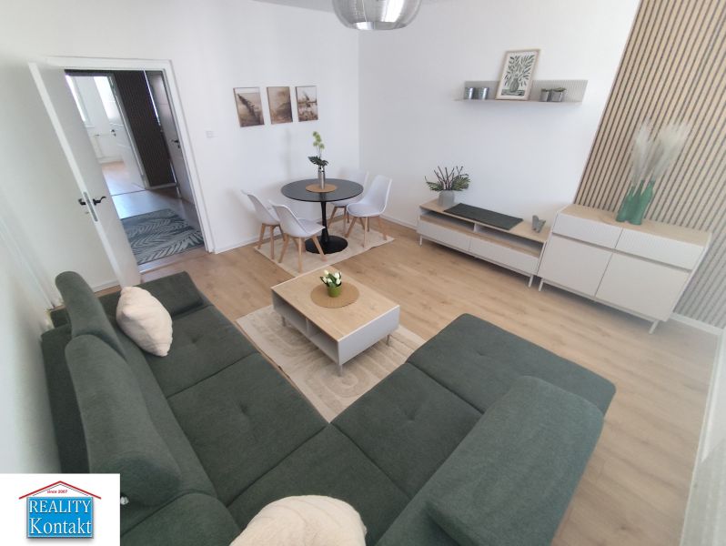 Living room in a 3-room apartment with a wooden decor floor, a sofa, and a dining table.
