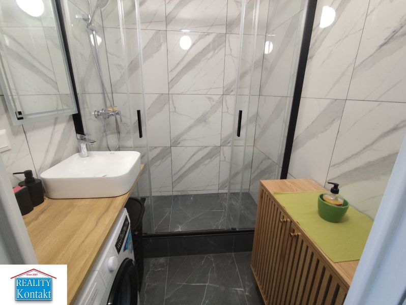 A bathroom with a shower, sink, and washing machine in a 3-room apartment.