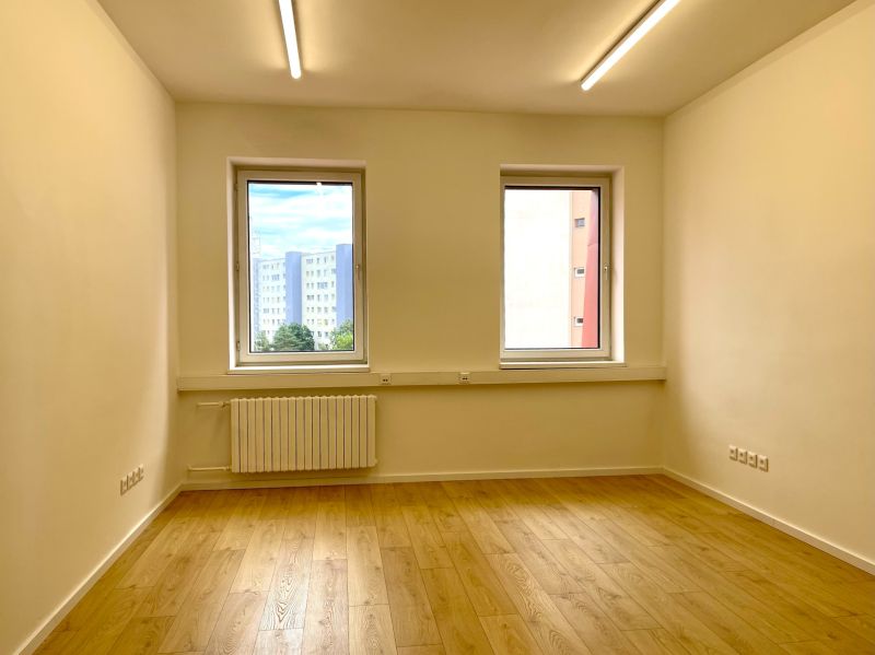 Empty office room with wood-patterned flooring and large windows.
