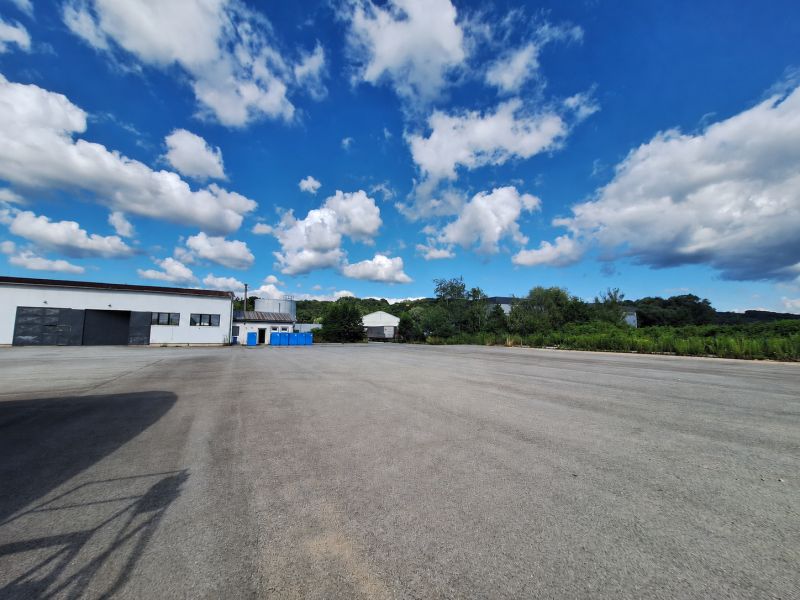 Warehouses and halls in Ličartovce with a paved area and blue containers under a blue sky.