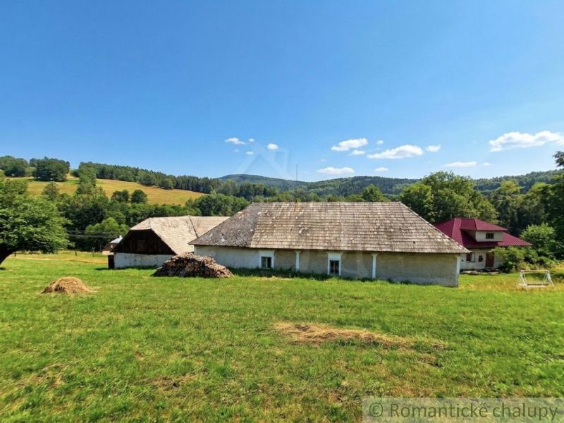 A family house in Dobroč surrounded by meadows and hills under a blue sky.