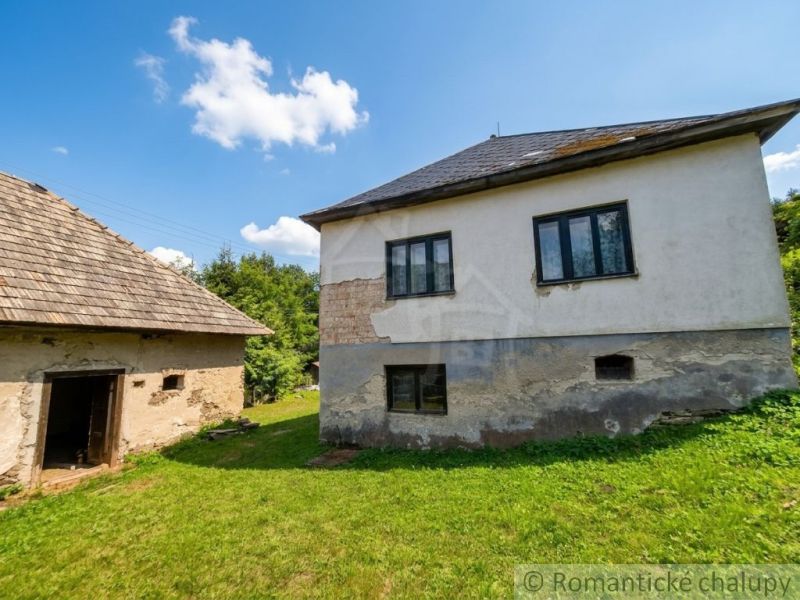 A family house in Dobroč with a concrete facade and a wooden shed in a green garden.