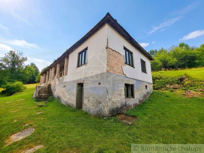 A family house in Dobroč with a damaged facade, built on a grassy slope.