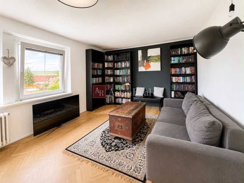 Living room in a 3-room apartment with a sofa, bookshelf, wood-patterned floor, and a large window.