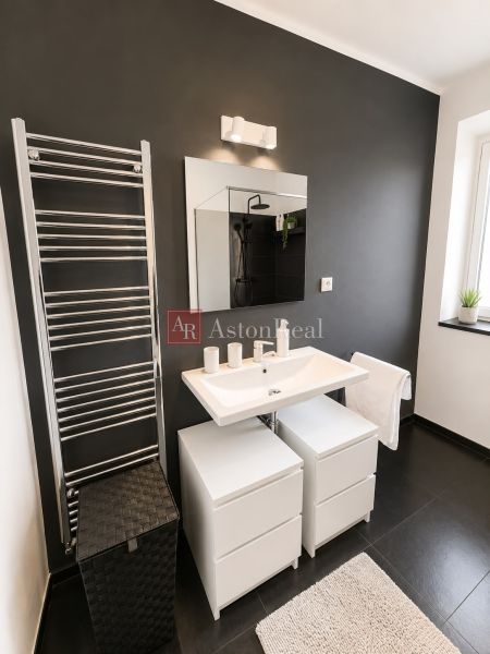 A bathroom in a 3-room apartment with a dark wall, a large mirror, and light furniture.