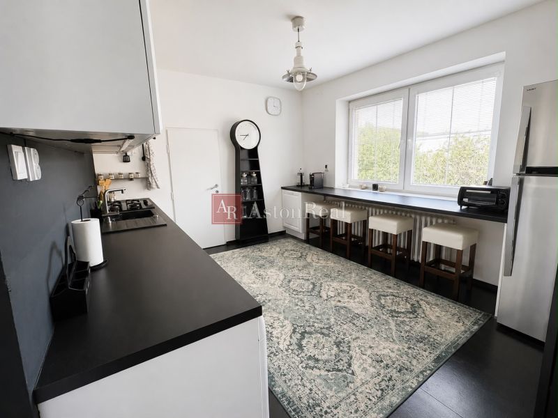 A kitchen in a 3-room apartment with a bar counter, dark countertops, and a large window.