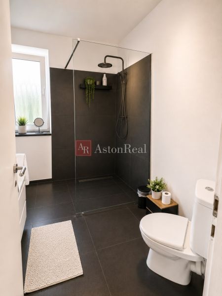 A bathroom in a three-room apartment with black tiles and a shower corner.