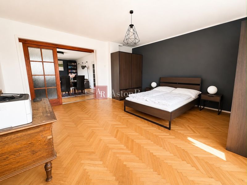 A bedroom in a 3-room apartment with a bed, wardrobe, and wooden decor flooring.