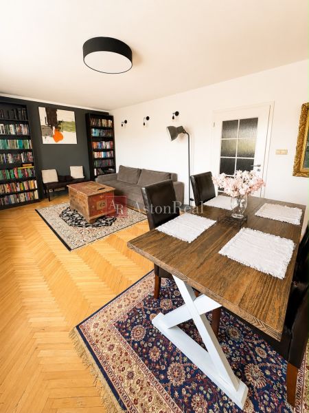 Living room in a three-room apartment with a wooden decor floor and a rich library.