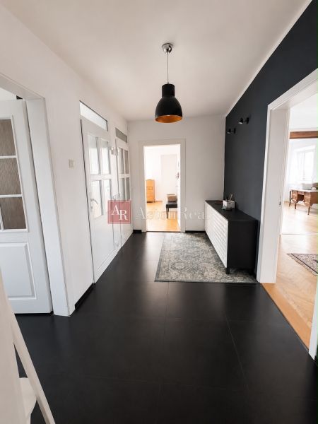 A hallway in a 3-room apartment with light walls, a black chandelier, and a dark floor.