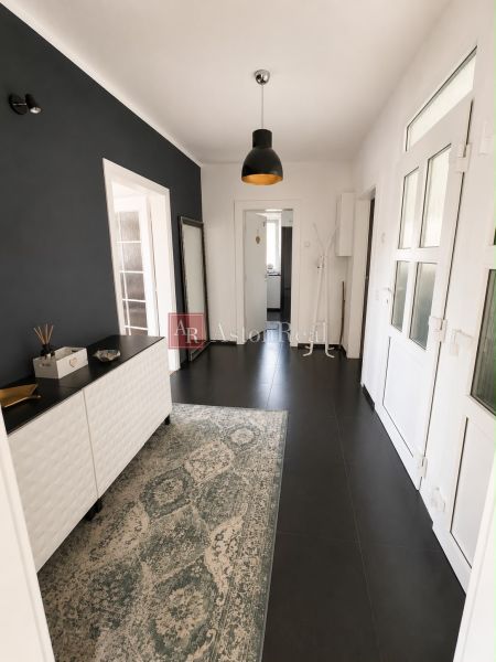 The hallway of a 3-room apartment with dark tiles and a carpet, complemented by wall lighting.