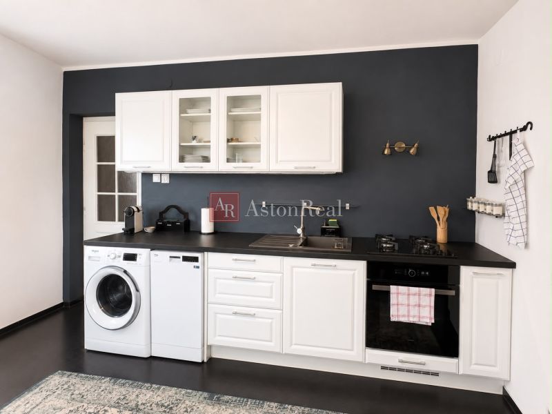 A kitchen in a 3-room apartment with a dark wall, white cabinets, and appliances.